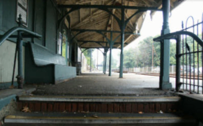 A picture of the westbound Devon Train Station platform looking East from just below ground level standing on the stairs of the underpass